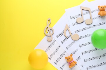 Baby songs. Music sheets, wooden notes, toy bears and balls on yellow background, top view with...