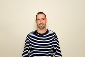 Hispanic man with beard wearing a striped sweater posing smiling on beige studio background.