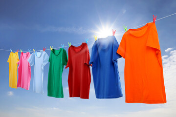 Colorful t-shirts drying on washing line against blue sky