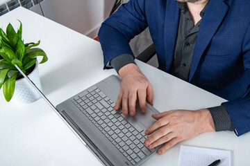 Fototapeta na wymiar Business executive in blue suit sitting at the desk with hands on the keyboard and notepad