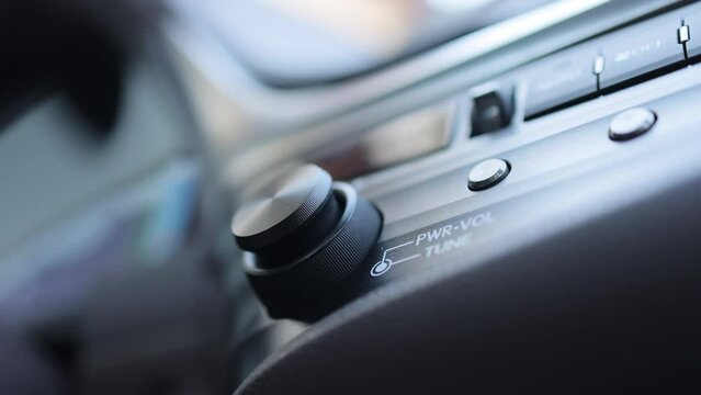 Car dashboard volume knob. Driver's hand adjusts volume control of car radio. Male hand control radio or music in car in motion. Turns up the volume of the music in the car.
