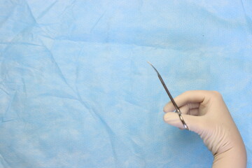 Surgical scissors in a surgeon hand wearing sterile gloves with a surgical surface with copy space...