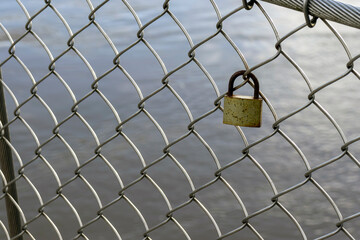 Valentine heart padlock attached to wire mesh fence. Love padlocks hanging on a bridge - 750190294