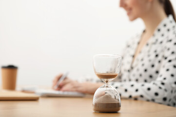 Hourglass with flowing sand on desk. Woman taking notes while using calculator indoors, selective...