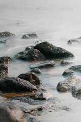 Cobblestones and rocks along the seacoast with smooth water through long exposure shot - 750193081