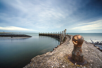 Urbex harbor in a round shape of weathered concrete with rusted boolders and rotten mooring posts and above a threatening cloudy sky - 750193444