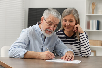 Happy senior couple signing Last Will and Testament indoors