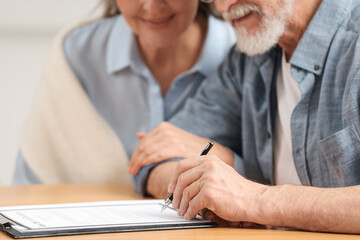 Senior couple signing Last Will and Testament indoors, closeup