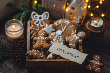 Concept of home christmas or new year celebration, family traditions. Assortment of gingerbread cookies with icing in a vintage wooden box on a window sill with atmospheric lights