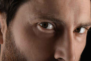 Evil eye. Man with scary eyes on black background, closeup