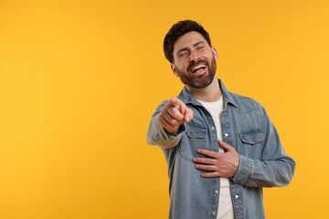 Handsome man pointing at something and laughing on yellow background. Space for text