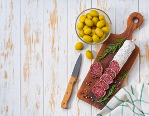 Spanish Fuet sausage salami with rosemary and olives on a wooden cutting board, top view.