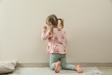 Little girl drawing on beige wall indoors, back view. Child`s art