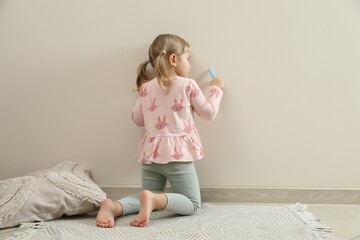 Little girl drawing on beige wall indoors, back view. Child`s art