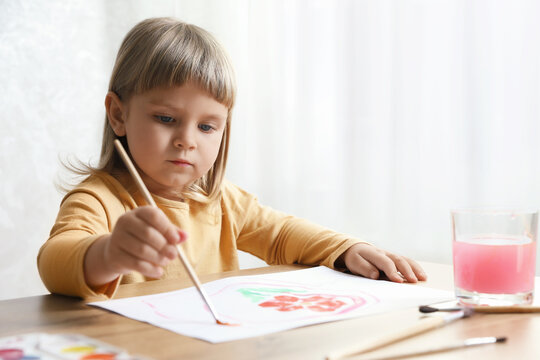 Cute little girl drawing with brush at wooden table indoors. Child`s art