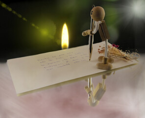 muñeco de madera escribiendo una carta de amor, junto a una vela