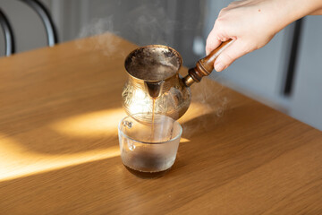 A woman pouring coffee into a cup from a copper Turkish coffee pot - obrazy, fototapety, plakaty