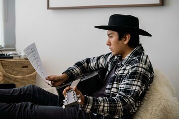Latin man playing acoustic guitar at home reading notes