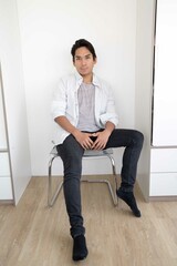 Latin man sitting on a chair against white wall