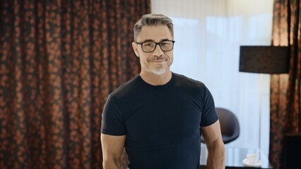 Adult male with glasses posing in a stylish room, showing confidence and sophistication. Portrait of happy mature man at home, smiling.