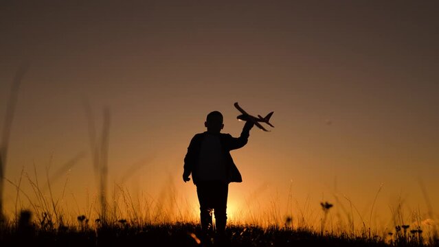 Happy Child boy plays with toy plane on field, sunset. Child boy wants to become pilot astronaut, Airplane flight. Children play with toy airplane. Teenager dreams of flying, becoming pilot. Childhood