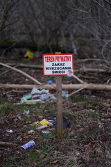 Znak Teren prywatny, zakaz wyrzucania śmieci, w tle leżące drzewa oraz śmieci