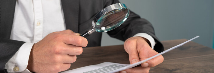 A man examines papers with a magnifying glass