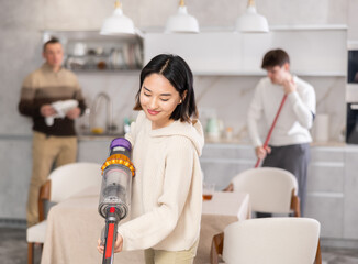 Girl vacuuming floor while his relatives help tidy up the room