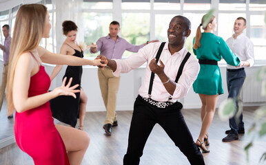 Woman in elegant evening dress dances incendiary boogie woogie with African American man partner...