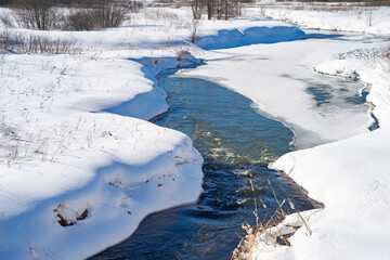 spring landscape with a river under ice and snowdrifts on the shore, March