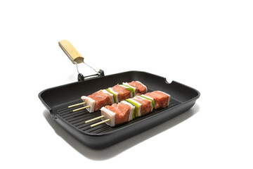 Raw meat and pepper skewers in a non-stick frying pan, isolated on a white background. Generally a skewer is made up of pieces of meat or fish interspersed with onion, pepper, mushrooms, etc.