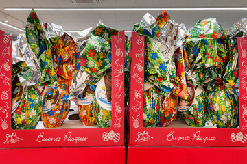 Easter eggs wrapped in colorful paper decorated with flower designs displayed in red boxes with inscription Buona Pasqua (Happy Easter) for sale in supermarket