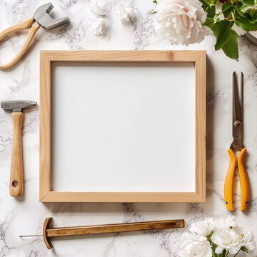 Still life of a wooden frame with white background, next to some white and pink flowers and some tools on marble background.