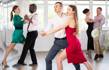 Dynamic young male and female attendees of dancing courses doing waltz in group