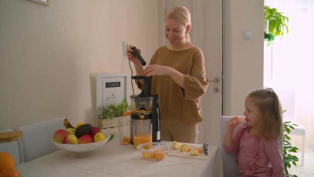 Mother and cute little daughter making healthy cold pressed raw juice together 