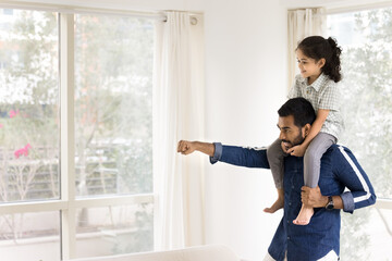 Sporty strong young Indian dad boxing with little daughter kid on shoulders, training power at...