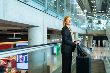 Asian businesswoman passenger with luggage using moving walkway go to check-in at airport terminal and waiting flight boarding. Business travel and air transportation concept.