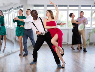 Elegant adult African American performing kizomba paired with attractive woman in red in studio class setting
