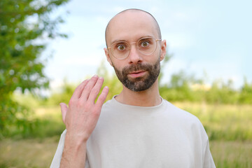 young charismatic man in beautiful gold-rimmed glasses, beige t-shirt looking at camera, male hand...