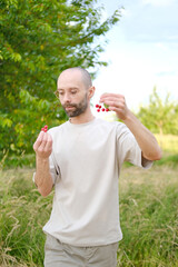 eating berries in garden, young man going to eat ripe red cherries, green garden in background,...