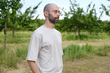 Satisfied young man 30-35 years old in light t-shirt, stylish glasses against natural background, Youth Culture and Stereotypes, younger generation, including clothing, accessories, outdoor activities