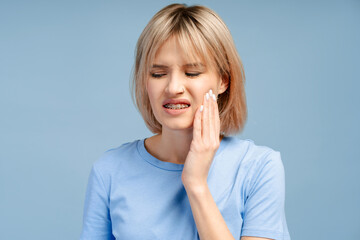 Sad upset young woman touching cheek, having toothache isolated on blue background