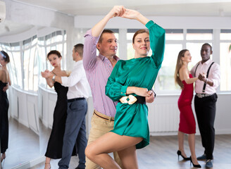 Fototapeta premium Happy man and woman in elegant clothes performing ballroom dance in dancing room during celebration or party