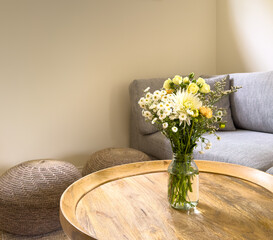 Fresh cut flowers in a jar on a round wooden coffee table in a lounge room - 750239819
