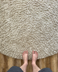 Top view of feet on a beige coloured shag pile floor with timber floor boards - 750239871