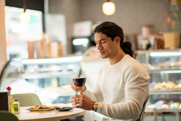 A brunette Hispanic man with long hair drinking coffee from a black mug.