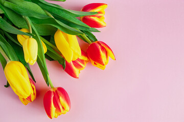 Bouquet of red and yellow tulips on pastel pink background.