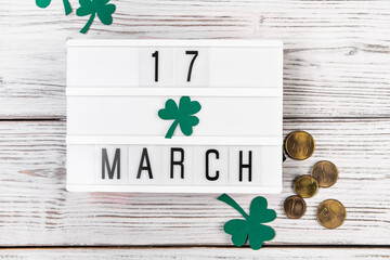 Flatlay for St. Patrick's Day. Gold coins and shamrock clover leaves on a white wooden background....