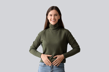 Young woman with healthy stomach on light background