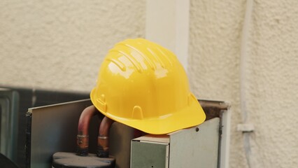 Extreme close up of yellow safety hardhat on top of out of order external air conditioner unit in...